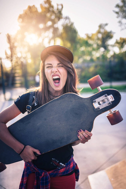 Χαριτωμένο κορίτσι της πόλης κρατώντας longboard στο πάρκο skate - Φωτογραφία, εικόνα