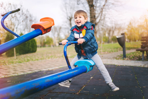 щасливий маленький хлопчик грає в парку на дитячому майданчику. дитина розважається на гойдалці. - Фото, зображення