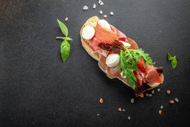 Spanish Tapas with cured Slices of jamon iberico ham with basil on a dark background. banner, menu, recipe place for text, top view. - Photo, image