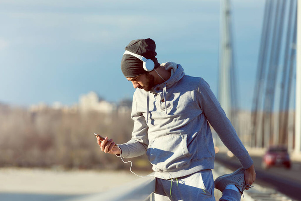 Man runner taking a break after intensive training outdoors, listening music on his mobile  - Fotó, kép
