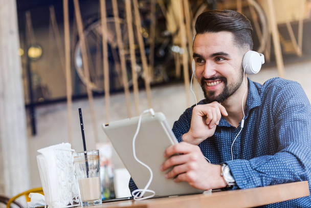 молодий чоловік з навушниками сидить за столом у кафе, використовуючи планшет
 - Фото, зображення