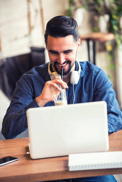 Cheerful Young Man with Beard Working on Laptop in Coffee Shop - 写真・画像