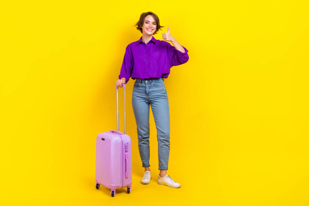 Full length photo of cute confident woman dressed purple shirt showing thumb up holding luggage isolated yellow color background. - Foto, Bild