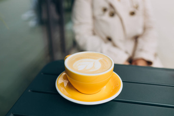 Een gele kop cappuccino met latte art. Koffie in gele beker op tafel in café. Geniet van het moment, neem een pauze. Begrip ontbijt - Foto, afbeelding