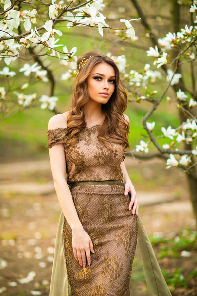 Spring Beautiful romantic girl in fashion long lace brown dress standing in blooming garden. Dreaming young model between magnolia trees. - Photo, Image