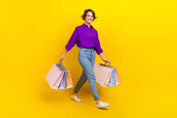 Full lenght photo of lovely young lady walk hold shopping bags wear trendy violet smart casual garment isolated on yellow color background. - Foto, Imagem