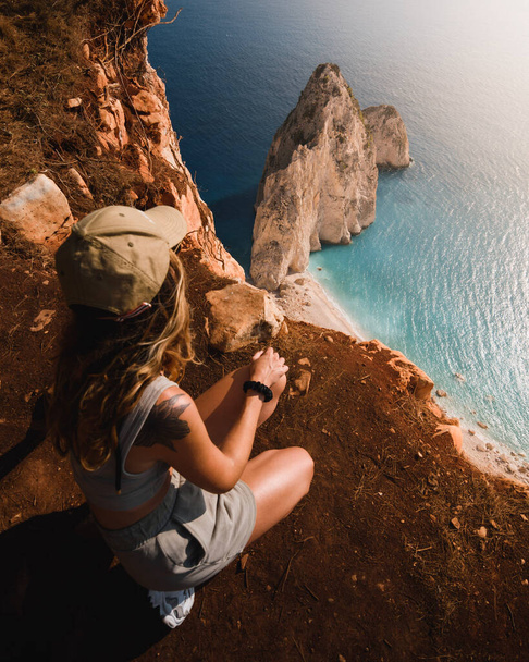 adventurous girl looking at the spectacular cliffs and turquoise waters of the Greek island of Zakhyntos during her sightseeing tour of the Ionian islands - Foto, imagen