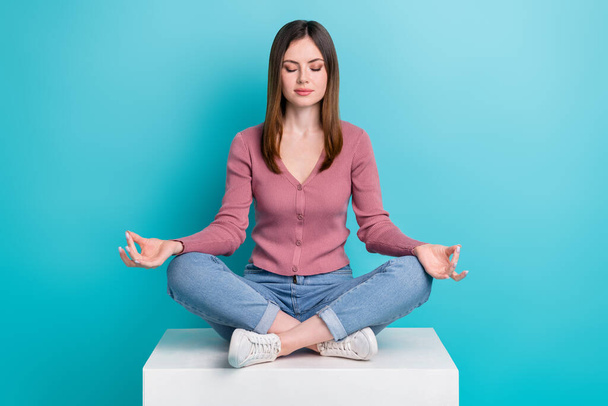 Full size photo of positive peaceful girl dressed stylish cardigan sit on cube concentrated meditation isolated on blue color background. - Foto, afbeelding