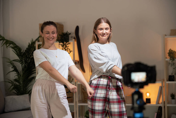 Twee jonge vrouwen in een pyjama die dansen opnemen op camera. Tieners maken 's nachts content voor social media. - Foto, afbeelding
