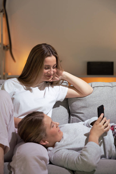 Two women using phone on sofa at night - Foto, Bild
