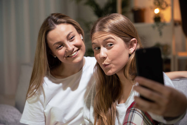 Due giovani donne che si fanno selfie a casa di notte. - Foto, immagini