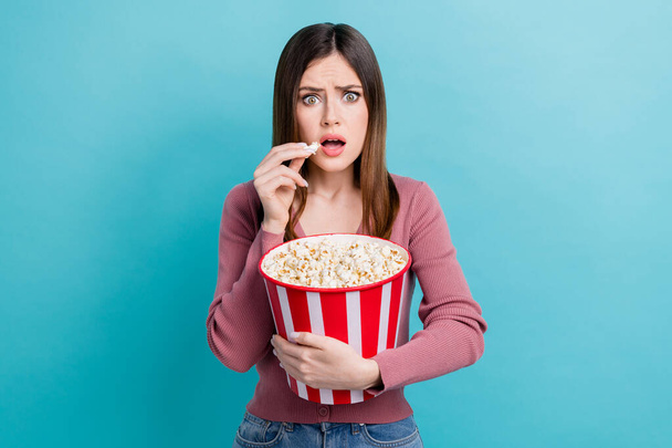Photo of adorable impressed girl straight hairdo dressed pink cardigan holding popcorn watching thriller isolated on blue color background. - Zdjęcie, obraz