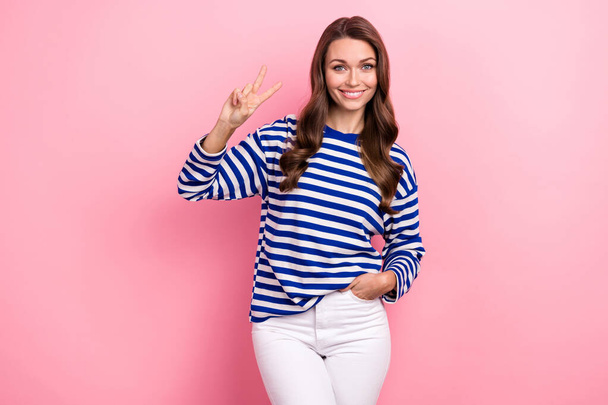 Photo of pleasant nice looking woman with wavy hairdo dressed striped shirt show v-sign arm in pocket isolated on pink color background. - Foto, Imagen