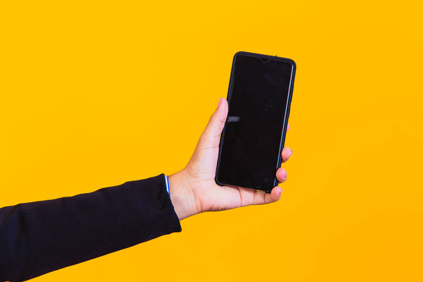 hand holding a cell phone on yellow background with space for text. - Фото, зображення
