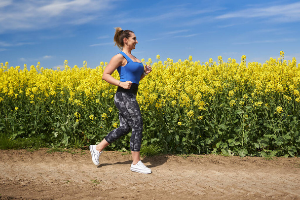 Plus velikost krásné latinské ženy jogging na polní cestě u canola pole - Fotografie, Obrázek