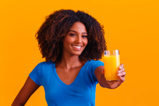 African american woman drinking orange juice in yellow background - Fotografie, Obrázek