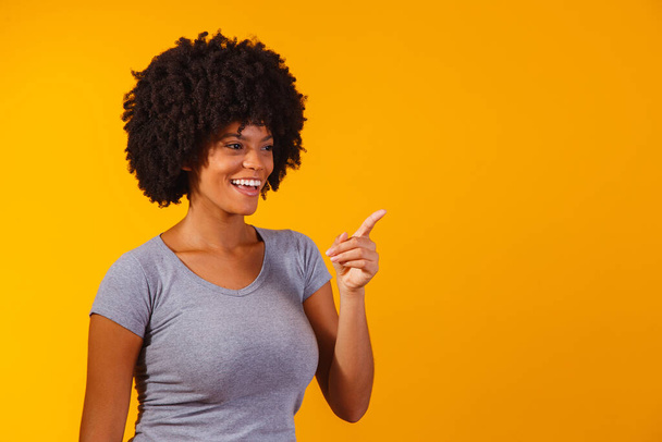 Afro woman pointing in yellow background with space for the text - Fotoğraf, Görsel
