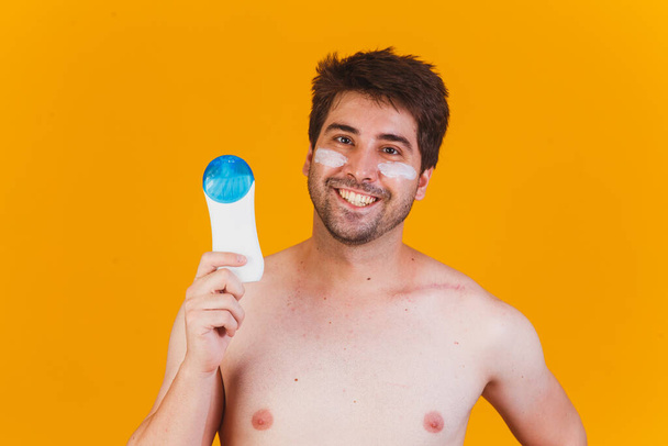 Handsome man with beard on vacation wearing swimwear holding bottle of sunscreen lotion looking positive and happy standing and smiling with a confident smile showing teeth - Foto, afbeelding