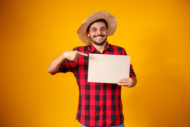 Brazilian man wearing typical clothes for the Festa Junina holding sign with space for text - Zdjęcie, obraz
