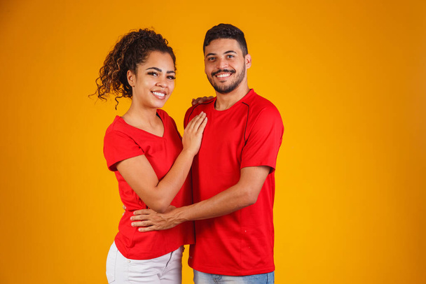 Portrait of content couple in basic clothing smiling at camera while woman putting her head on male shoulder isolated over yellow background he is surprised and happy - Fotografie, Obrázek