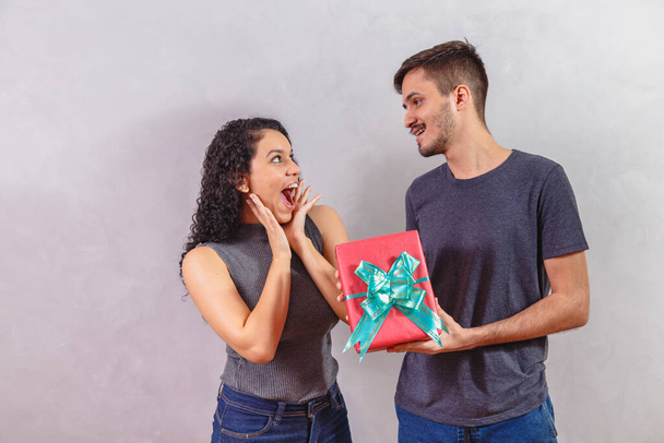 Portrait of a beautiful young couple on gray background with a gift. - Foto, imagen