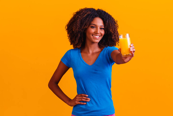 African american woman drinking orange juice in yellow background - 写真・画像