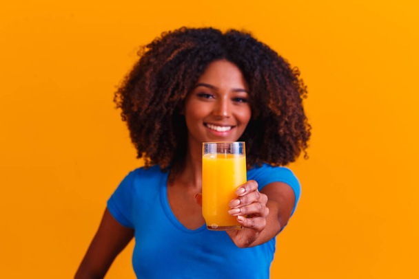 Mujer afroamericana bebiendo jugo de naranja en fondo amarillo - Foto, imagen