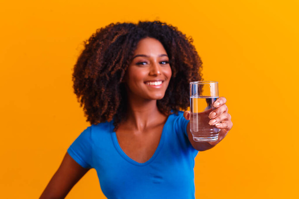 young black woman drinking water in yellow background. Young girl with glass of water - Foto, Imagen