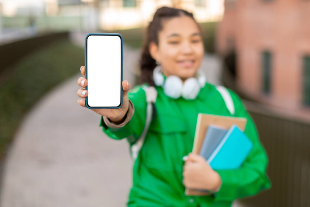 tiener student meisje demonstreren blanco smartphone op camera, poseren op college campus in de buurt van universiteit gebouw buiten, dame reclame educatieve app of website, mockup - Foto, afbeelding