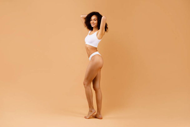 Body care concept. Slim black lady with ideal body shape posing in white underwear isolated on beige studio background, full length shot, copy space - Fotoğraf, Görsel