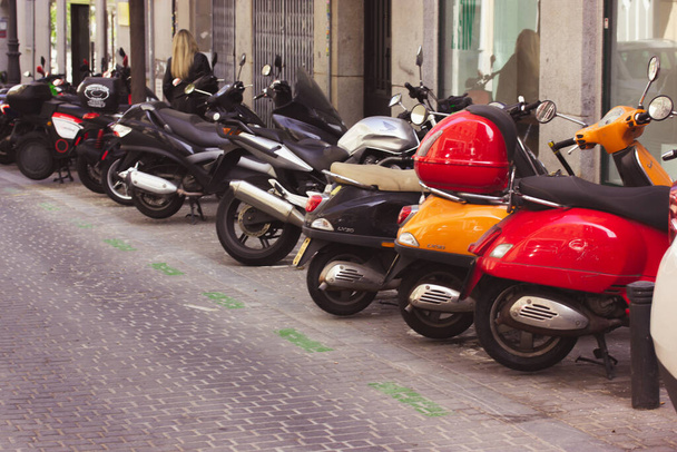 Madrid, Spain. May 1, 2022 Multicolored red and orange scooters, motorcycles parked in a row on an old city street. Parking lot for bikes. Ecological vehicle, classic motorbikes outdoors. Urban life. - 写真・画像