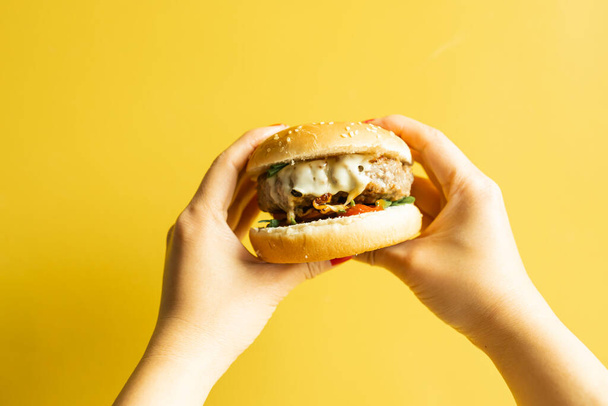 Hot tasty burger in female hand on yellow background. - Фото, изображение