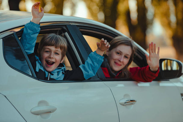 Happy mother and son waving hands from car window - Фото, изображение