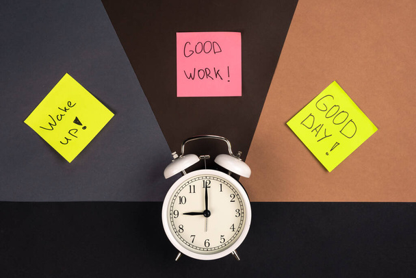 Relógio de alarme branco e adesivos coloridos com inscrições motivacionais em um fundo de papel, vista superior. - Foto, Imagem