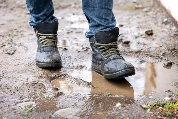 A man in jeans and boots walks through the swamp in rainy weather, in the countryside, legs close up. - Photo, Image