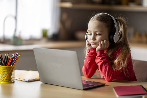 Verkko-oppimisongelmia. Tylsistynyt pieni tyttö langattomissa kuulokkeissa katsomalla kannettavaa tietokonetta, järkyttynyt esiteini-ikäinen nainen lapsi tutkimus tietokoneella kotona, kotitehtävät, etäopetusongelmat - Valokuva, kuva