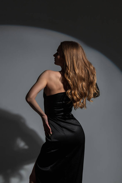 Hermosa señora de la moda elegante con el pelo rizado en un elegante vestido negro elegante posando en el estudio sobre un fondo oscuro con luz circular - Foto, Imagen