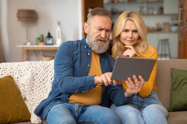 Yenilik Dokunuşu. Bilmece oynayan yaşlı çift dijital tablet kullanıyor evde otururken zor zaman geçiriyorlar ve internette geziniyorlar. Yaşlılar Çevrimiçi Teknoloji ve Gadget Olasılıklarını Keşfediyor - Fotoğraf, Görsel