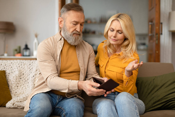 Financial Struggle. Unhappy Senior European Couple Looking At Empty Wallet With No Money, Suffering From Economic Crisis Sitting On Sofa At Home. Distressed Spouses Facing Finance Hardship Together - Photo, Image