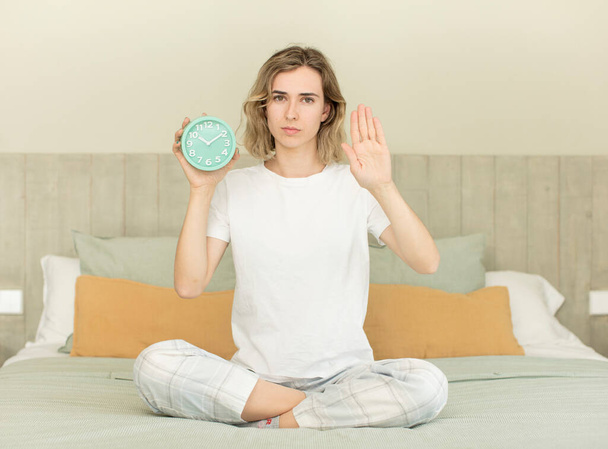 pretty woman looking serious showing open palm making stop gesture alarm clock concept - 写真・画像