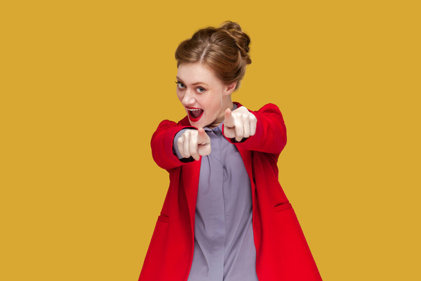 Portrait of excited flirting woman with red lips standing pointing at you, looking at camera with positive expression, wearing red jacket. Indoor studio shot isolated on yellow background. - Zdjęcie, obraz