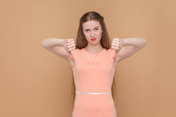 Portrait of dissatisfied unhappy pretty woman with long hair standing showing dislike gesture, doesn't like service, wearing elegant dress. Indoor studio shot isolated on brown background. - Foto, Bild