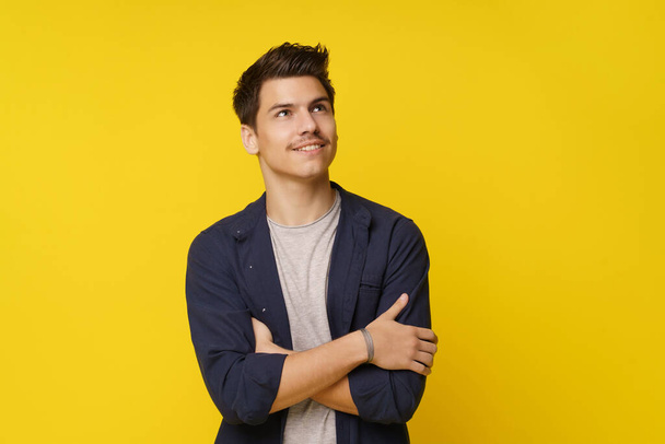 Young man in contemplative pose, with his hands crossed and eyes closed, lost in thought and dreaming of his future. Shot against a bright yellow background, the image conveys sense of optimism and - Foto, afbeelding