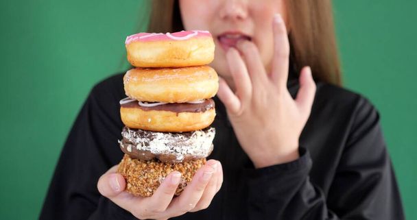Nahaufnahme einer Frau, die isoliert vor grünem Hintergrund posiert und zwischen Donuts-Süßigkeiten wählt - Foto, Bild