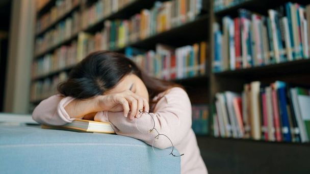 zmęczona Azji student dziewczyna w okulary śpi na książki w bibliotece - Zdjęcie, obraz