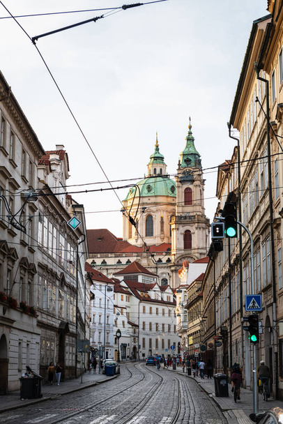 PRAGUE, CZECH REPUBLIC - AUGUST 24, 2022: Narrow street in Mala Strana district in Prague with St Nicholas Church emerging in the background. - Фото, зображення