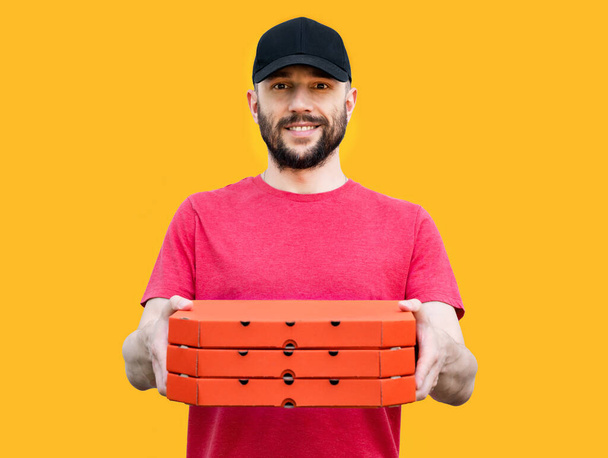 Uśmiechnięty dostawca pizzy trzymający pudełka po pizzy na żółtym tle. Dostawa pizzy. Skupienie selektywne. - Zdjęcie, obraz