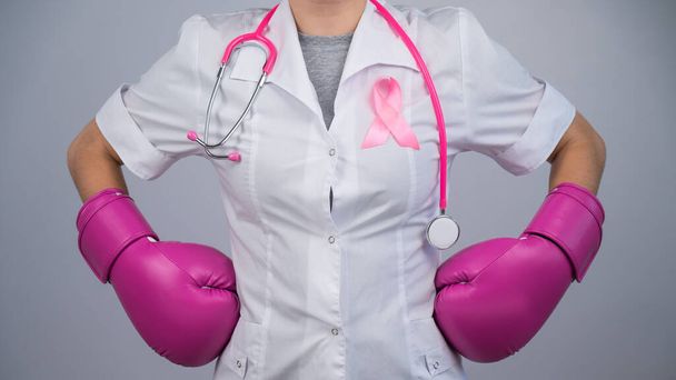 Faceless female doctor in pink boxing gloves with a pink ribbon on a gray background. Fight against breast cancer - Φωτογραφία, εικόνα