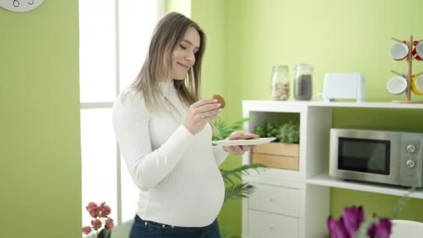 Молодая беременная женщина, нюхающая печенье, страдает тошнотой в столовой - Кадры, видео