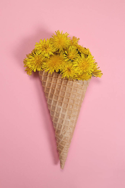Bouquet di fiori di tarassaco in un cono di cialda gelato su sfondo rosa. Orientamento verticale - Foto, immagini